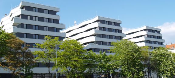 Weiße Treppenartig abgesetzte Fassade mit rundum Balkonen Straßenseite mit Baumallee © Gesiba